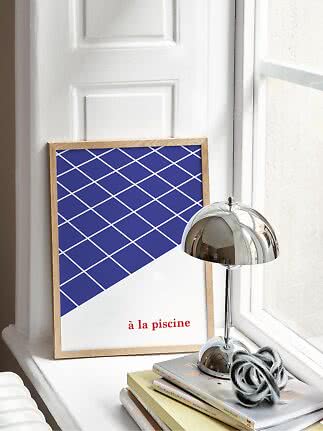 Framed blue and white graphic poster on a windowsill beside a chrome table lamp