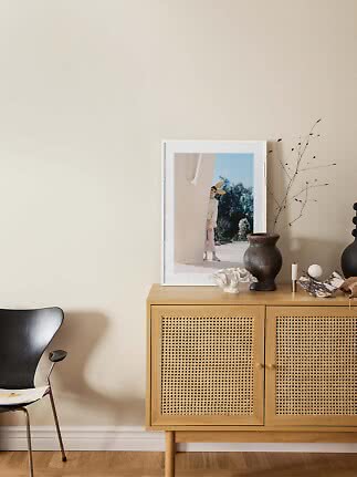 Sideboard aus hellem Holz mit Geflechtüren, Vase, Deko und gerahmtem Bild vor beiger Wand