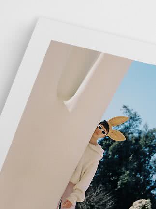 Person schaut hinter einer Wand hervor mit Sonnenbrille und Strohhut mit Hasenohren