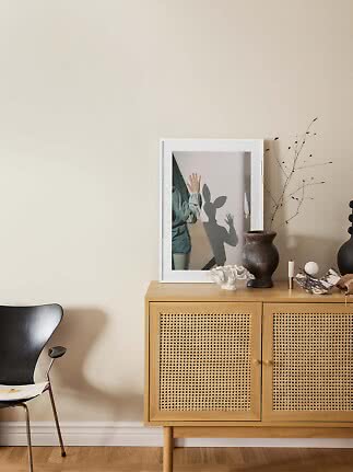 Sideboard aus hellem Holz mit Geflechttüren, Vase, Kerzenhalter und gerahmtem Bild vor beiger Wand