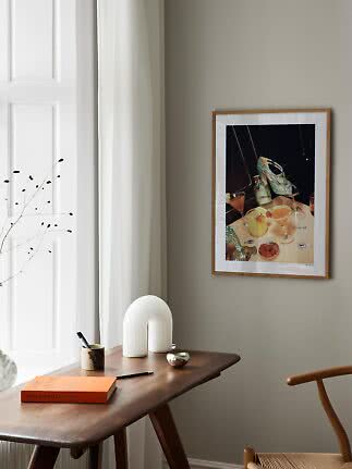 Poster incorniciato con cocktail e tacchi scintillanti sopra una scrivania in legno in una stanza luminosa