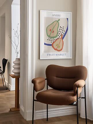 Fauteuil brun près d’un mur avec affiche de fruits encadrée et vase sur table étroite