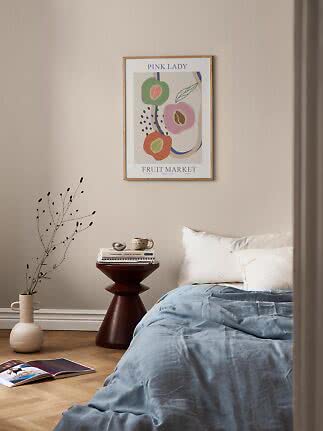 Affiche fruitée colorée encadrée au-dessus d’un lit dans une chambre au linge bleu