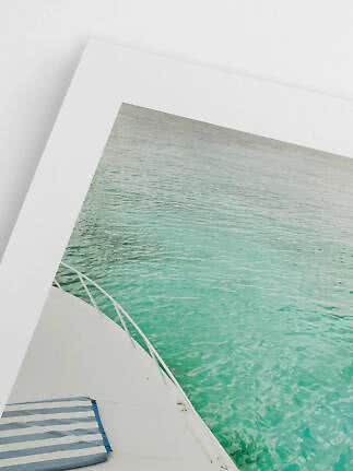 Foto enmarcada de un barco sobre agua turquesa apoyada en una pared blanca