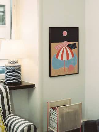 Colorful abstract framed poster on wall beside a table lamp and magazine rack