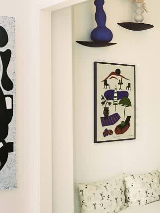 Cozy corner with framed art, wall shelves with vases, and a sofa with patterned cushions