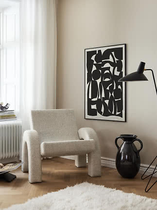 Modern cream bouclé armchair beside a black floor lamp and abstract black-and-white poster