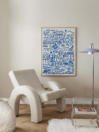 Blue and white framed poster on a beige wall above a cream lounge chair beside a floor lamp
