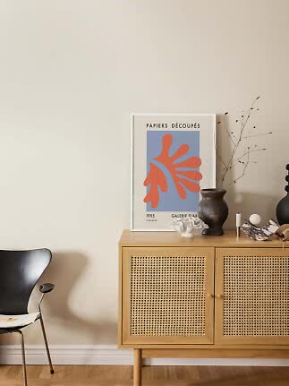 Skænk i lyst træ med fletlåger, vase, kunstplakat og stol ved beige væg