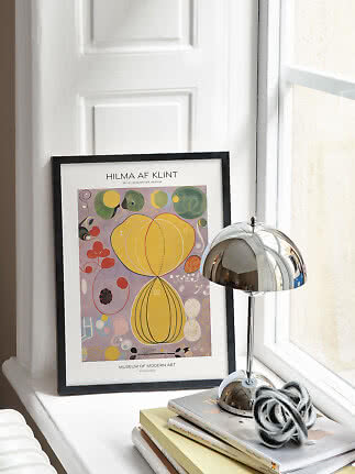 Oprawiony plakat Hilmy af Klint na parapecie obok chromowanej lampy i książek