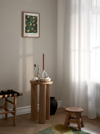 Lyst hjørne med rundt træbord, lysestage, små dekorationer og botanisk plakat på væggen