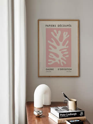 Framed pink art print above a wooden table with books, a sculptural vase, and a mug