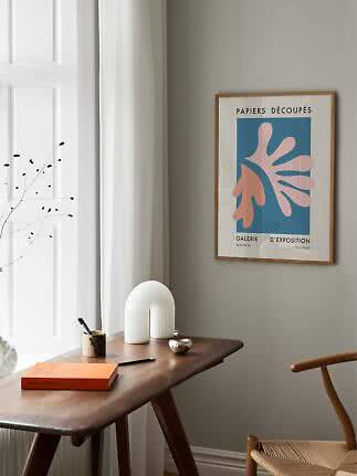 Gerahmtes abstraktes Poster über einem Holzschreibtisch am Fenster in hellem, minimalistischem Raum