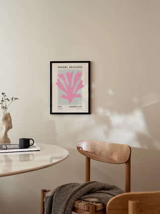 Framed art print with pink organic motif on beige wall above table and wooden chair