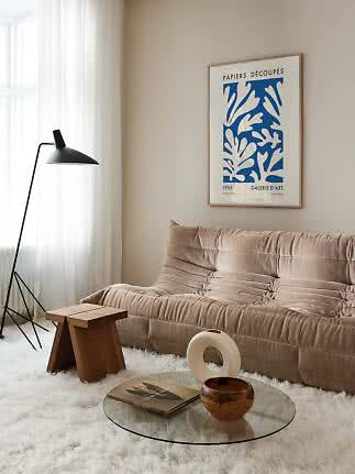 Cozy living room with beige sofa, black floor lamp, glass coffee table, and blue wall art poster