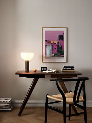 Dark wood desk with chair, table lamp, books and framed photo against a light wall