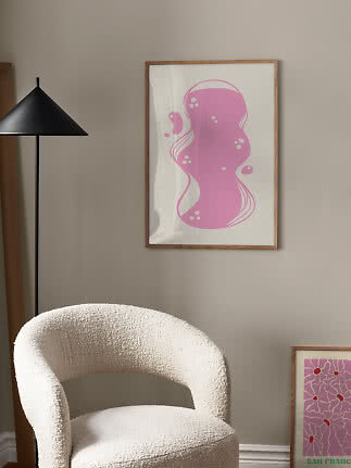 Affiche abstraite encadrée à motif rose sur mur beige au-dessus d'un fauteuil bouclé blanc.