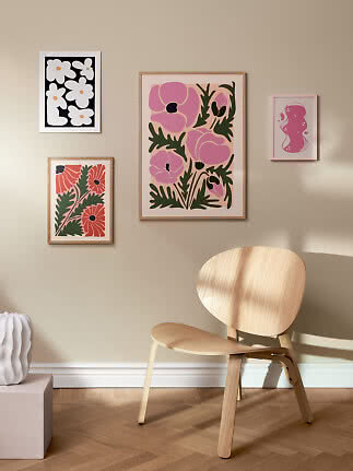 Silla de madera clara junto a pared beige con cuatro láminas florales enmarcadas en rosa y coral