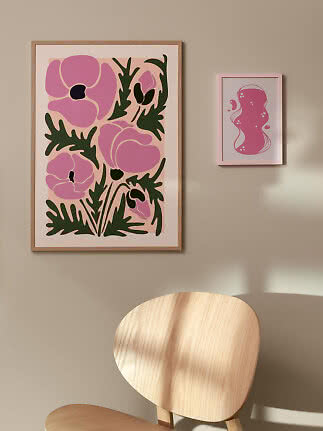 Dos láminas artísticas rosas enmarcadas en una pared beige sobre sillas de madera clara