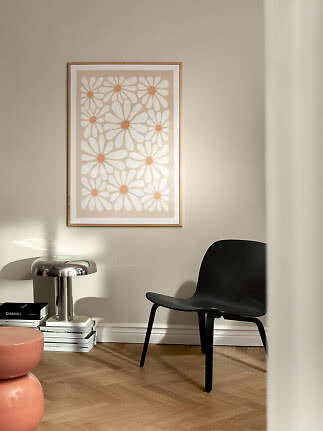 Indrammet blomsterplakat i beige og hvid på væg over sort stol i moderne stue