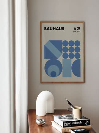 Framed Bauhaus poster with blue geometric shapes on a beige wall above a wooden table