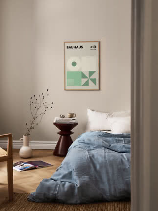 Oprawiony plakat Bauhaus z zielonymi geometrycznymi kształtami nad łóżkiem w spokojnej sypialni