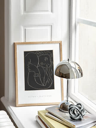 Poster di Matisse incorniciato su davanzale accanto a lampada da tavolo cromata e libri impilati