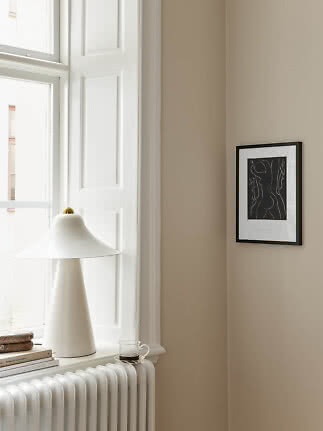 White table lamp on a windowsill by a bright window, with books, cup and framed art on a beige wall