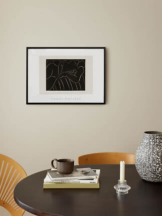 Indrammet Henri Matisse-plakat over mørkt spisebord med bøger, krus, lysestage og stor vase