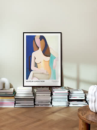 Framed art poster of an abstract seated woman, leaning against a wall above stacked books