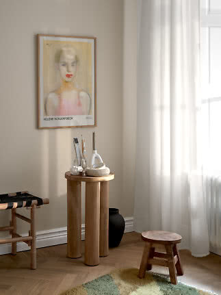 Poster d’arte incorniciato con ritratto di donna su parete beige sopra un piccolo tavolo in legno