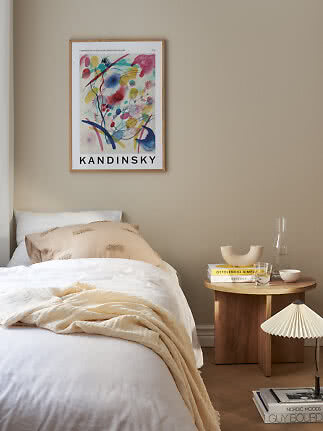 Inramad Kandinsky-poster med färgstarkt abstrakt motiv ovanför en säng i ett beige sovrum