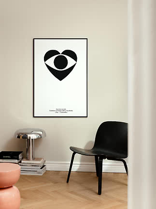 Minimalistisches Poster mit schwarzem Augenmotiv im schwarzen Rahmen an heller Wand über Stuhl