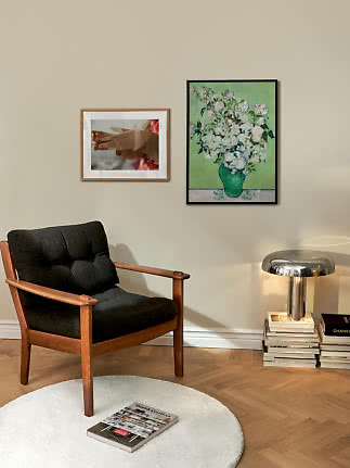 Coin cosy avec fauteuil en bois, deux affiches encadrées et lampe chromée sur des livres