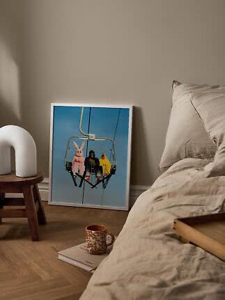 Poster incorniciato con figure mascherate su una seggiovia accanto al letto in una camera tranquilla