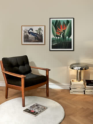 Cozy corner with wooden armchair, round white rug, book, table lamp, and two framed wall prints