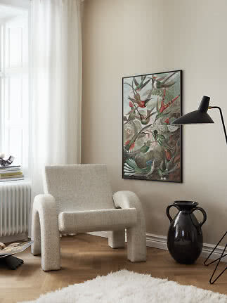 Heller Bouclé-Sessel an der Wand mit Vogelposter, schwarzer Stehlampe und dunkler Vase
