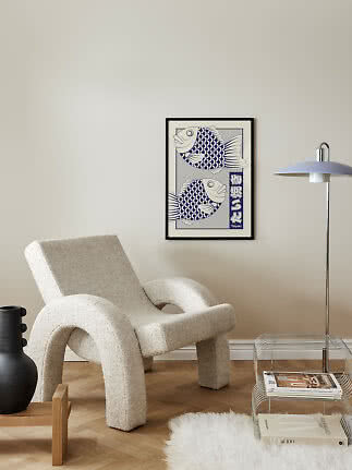 Blå og hvid plakat med to fisk i sort ramme på beige væg over en lænestol