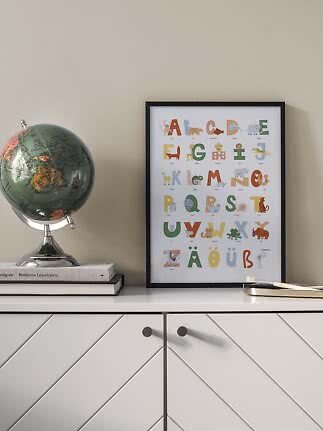 Framed animal alphabet poster on a cabinet beside a globe and books