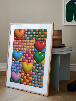 Framed colorful art print with large hearts and checker pattern, leaning by a side table