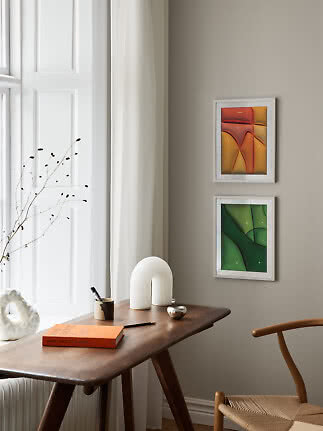 Gemütlicher Holzschreibtisch am Fenster mit Stuhl, Vase, Buch und zwei abstrakten Bildern an der Wand
