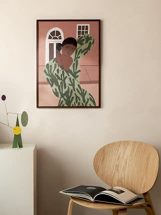 Framed poster of a stylized woman in a green patterned dress on a beige wall above a wooden chair