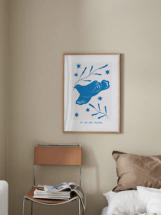 Framed poster with blue bird and stars on beige wall above chair beside bed
