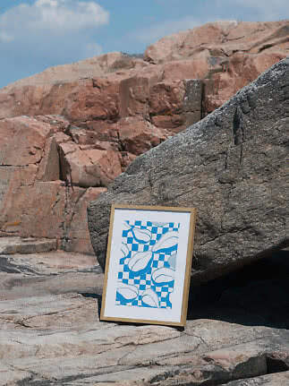 Framed blue and white abstract print leaning against a large rock outdoors