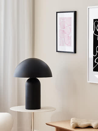 Black table lamp with dome shade on a small round side table in a bright modern room