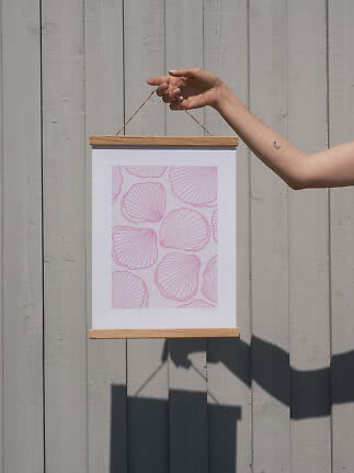 Hand holding hanging poster with pink shell pattern in wooden frame against gray wood wall