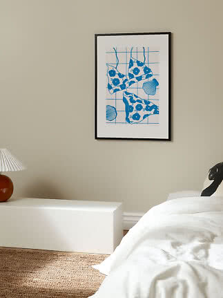 Framed blue and white swimsuit poster hanging above a white bedside table in a bedroom