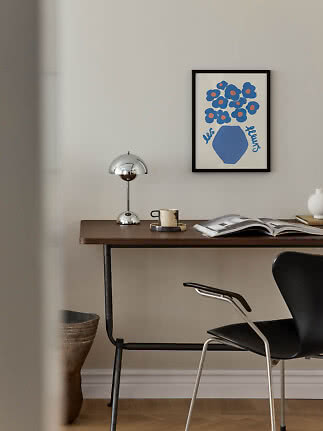 Bureau moderne avec lampe chromée, tasse, livre ouvert et affiche florale encadrée au mur