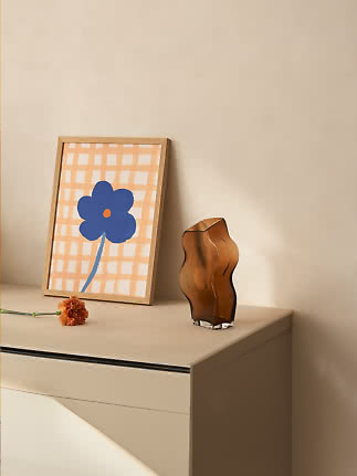 Vase en verre brun ondulé sur une commode, avec cadre fleuri et œillet orange