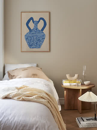 Chambre cosy avec lit blanc, table de chevet en bois et tableau vase bleu sur mur beige